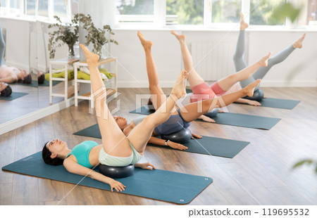 Together with students, teacher lies with fitball under her buttocks and performs swings with feet Together with students, teacher lies with fitball under her buttocks and performs swings with feet 119695532