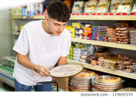 in supermarket in department of semi-finished products, man chooses pizza in supermarket in department of semi-finished products, man chooses pizza 119695550