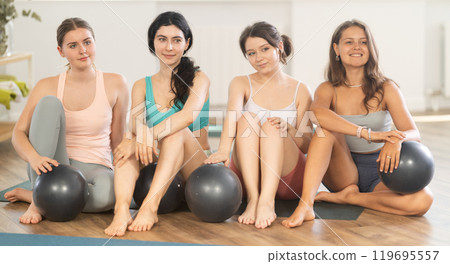 Young girl yoga instructor in company of female students poses for group photo with fitness balls 119695557