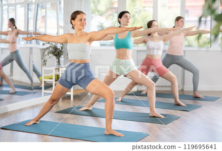 Young girl performing Virabhadrasana asana during group yoga training 119695641