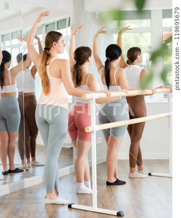 Young girl practicing third position holding by ballet barre 119695679