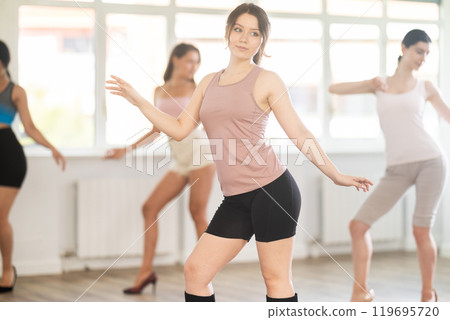 During lesson, girl learn to move and perform dance in heels with women companions During lesson, girl learn to move and perform dance in heels with women companions 119695720