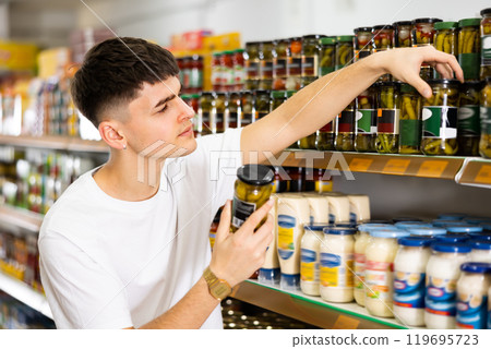 young man buys jar of canned vegetables in grocery supermarket 119695723