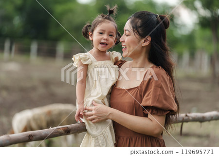 cheerful mother holding toddler baby girl at sheep farm cheerful mother holding toddler baby girl at sheep farm 119695771
