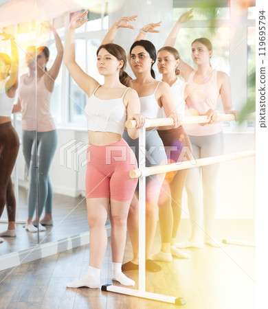 Young girl practicing fourth position holding by ballet barre 119695794