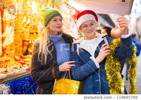 Happy mother with daughter choosing Christmas decoration and balls at Christmas market Happy mother with daughter choosing Christmas decoration and balls at Christmas market 119695798