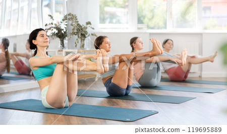 Young girl teaches yoga lesson, shows students technique of performing Paripurna Navasana asana 119695889
