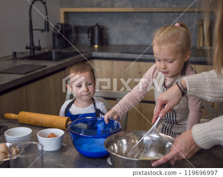 Mother and her two kids bonding in a contemporary kitchen, mixing cookie dough, adding ingredients, and enjoying family cooking time, concept of cooking food from dough, cook at home 119696997