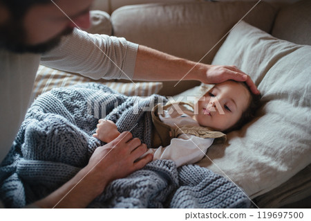 Father taking care of sick girl with fever and cold at home. Daughter lying on sofa, feeling tired. Father taking care of sick girl with fever and cold at home. Daughter lying on sofa, feeling tired. 119697500