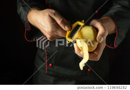Chef peels raw potatoes with a vegetable peeler. Preparing to cook potato dish or mashed potatoes by the hands of the cook 119698282