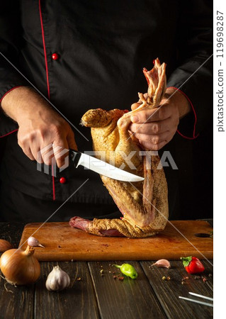 In a warm kitchen, a chef expertly holds a duck while cutting it with a sharp knife, surrounded by fresh vegetables and spices, showcasing culinary skills and preparation techniques 119698287