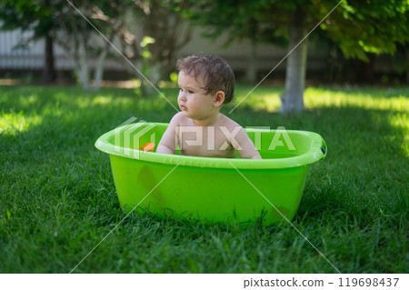 Cute baby boy bathes in a basin outdoors in summer. Cute baby boy bathes in a basin outdoors in summer. 119698437