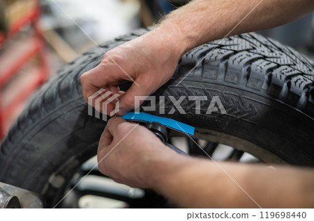 A mechanic attaches balancing weights to a wheel.  119698440