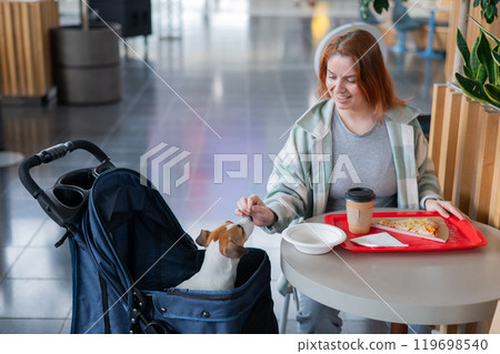 Caucasian woman having lunch in a cafe with her Jack Russell terrier dog in a stroller. Caucasian woman having lunch in a cafe with her Jack Russell terrier dog in a stroller. 119698540