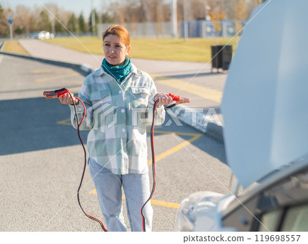Woman holding clamps for charging a car battery.  119698557