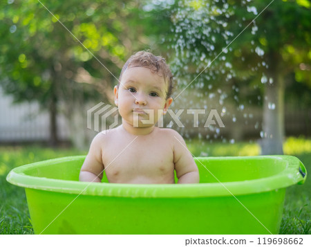 Cute baby boy bathes in a basin outdoors in summer. 119698662