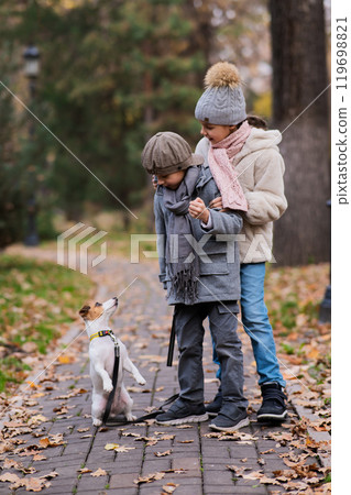 Caucasian children walk with a Jack Russell Terrier dog in the autumn park. 119698821