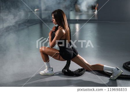 Caucasian woman holds the ropes and does a lunge in the exercise machine. Caucasian woman holds the ropes and does a lunge in the exercise machine. 119698833