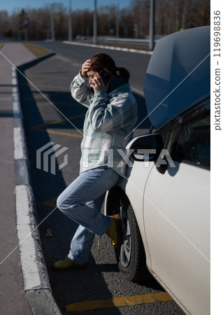 Sad Caucasian woman calling on phone while standing near car with open hood.  119698836