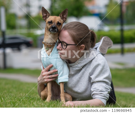Young Caucasian woman lying on the lawn while walking with a small dog. Young Caucasian woman lying on the lawn while walking with a small dog. 119698945