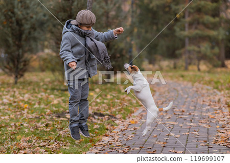 Caucasian boy playing with a dog for a walk in the autumn park.  119699107