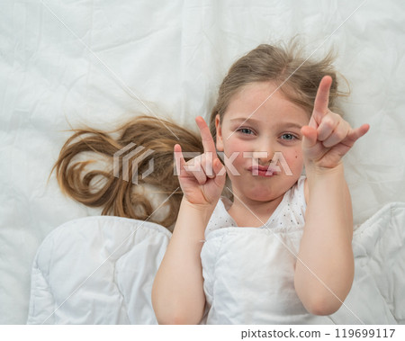 Top view of a grimacing little girl lying in bed.  119699117