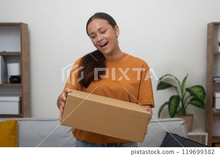 Excitement radiates from lady as she receives her desired package, a testament to the joy of internet shopping Excitement radiates from lady as she receives her desired package, a testament to the joy of internet shopping 119699382