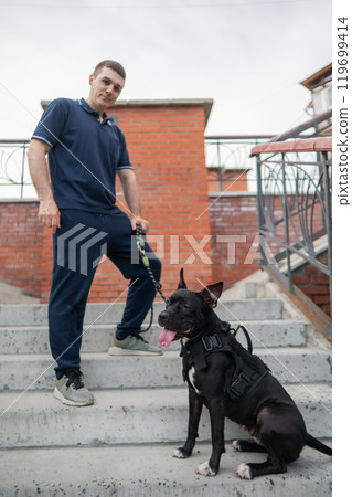 Caucasian man with a pitbull terrier dog sitting on the stairs. Caucasian man with a pitbull terrier dog sitting on the stairs. 119699414
