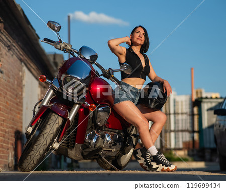 Brunette woman in shorts posing on a red motorcycle. Brunette woman in shorts posing on a red motorcycle. 119699434