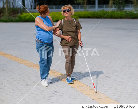 Caucasian pregnant woman leading blind elderly lady outdoors. Caucasian pregnant woman leading blind elderly lady outdoors. 119699460