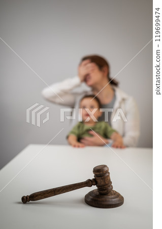 Caucasian woman crying with baby in her arms behind judge's gavel divorce. Caucasian woman crying with baby in her arms behind judge's gavel divorce. 119699474