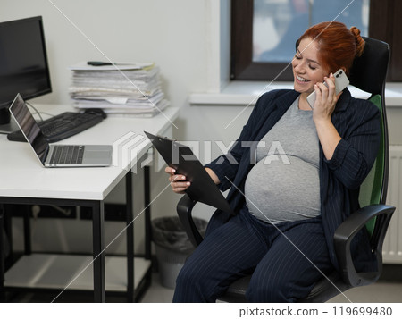 Pregnant woman using mobile phone and holding paper tablet in office. Pregnant woman using mobile phone and holding paper tablet in office. 119699480