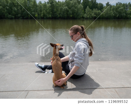 Young Caucasian woman and cute little dog walking on the river bank.  119699532