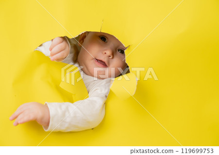 Cute Caucasian baby sticking out of a hole in a paper yellow background.  119699753