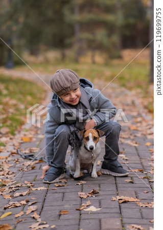 Caucasian boy walking with dog jack russell terrier in autumn park. 119699755