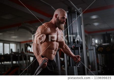 Bald Caucasian bodybuilder training chest using cable crossover in gym. Bald Caucasian bodybuilder training chest using cable crossover in gym. 119699835