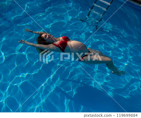 Top view of pregnant woman floating in pool in red bikini.  119699884