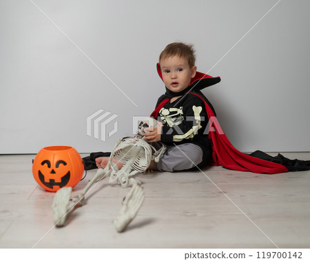 Little Caucasian boy in Dracula costume holding skull on white background.  119700142