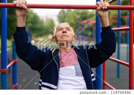 Senior man hanging from pullup bar outoors Senior man hanging from pullup bar outoors 119700486