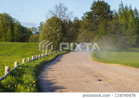 Empty rural road with wooden fence on the roadside and road dust 119700876