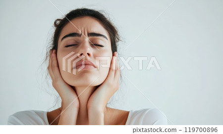 Young woman is holding her neck with her hands, her eyes closed in pain, suggesting she is suffering from a stiff neck or a migraine 119700896