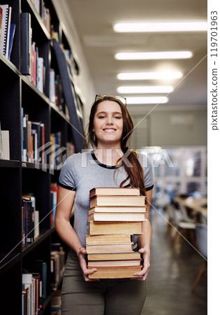 Woman, student with stack of books in library and research for project, studying and learn on university campus. Young female person smile in portrait, education and scholarship with course material 119701963