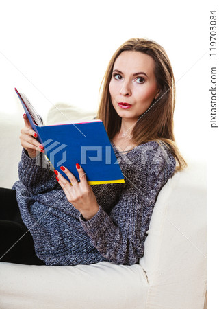 Woman sitting on couch reading book at home 119703084