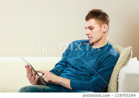 Young man with tablet sitting on couch at home 119703264