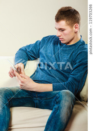 Young man with digital tablet sitting on couch Young man with digital tablet sitting on couch 119703266