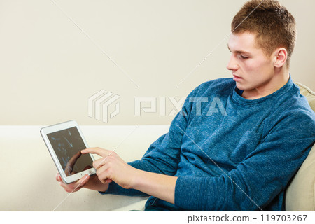 Young man with digital tablet sitting on couch Young man with digital tablet sitting on couch 119703267