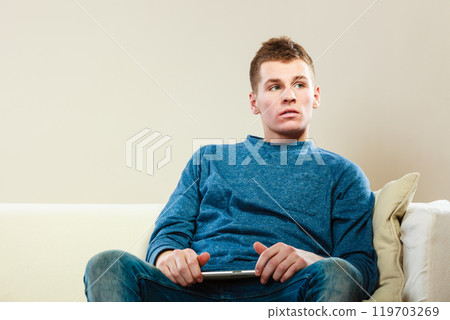 Young man with digital tablet sitting on couch Young man with digital tablet sitting on couch 119703269