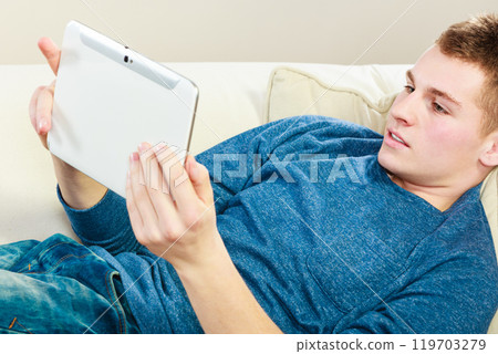 Young man with digital tablet laying on couch 119703279