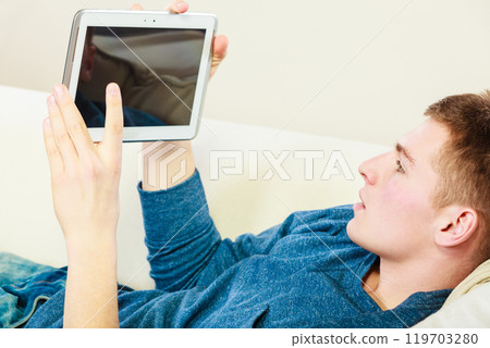 Young man with digital tablet laying on couch Young man with digital tablet laying on couch 119703280