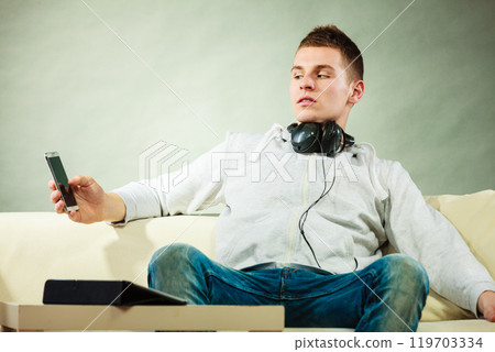 man on couch with headphones smartphone and tablet 119703334